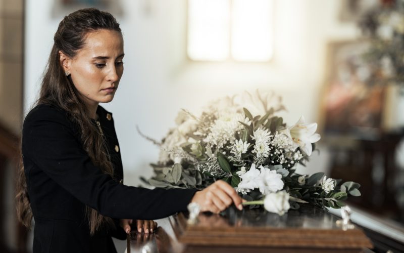 Funeral, sad and woman with flower on coffin after loss of a loved one, family or friend. Grief, de.